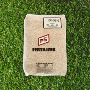 A bag labeled "FS Fertilizer" rests on lush green grass, with text displaying product details and numbers 5-20-20.