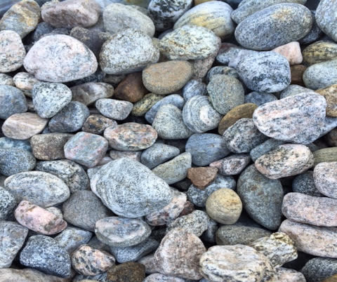 Close-up of a collection of smooth, multicolored pebbles, showcasing various shades of gray, pink, and brown, with a textured, natural surface.