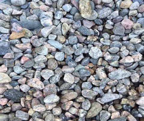 A close-up of variously colored small pebbles and rocks, displaying a mix of textures and shades of gray, pink, and brown.