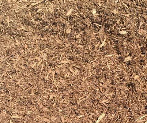 The image shows a close-up of brown wood chips or mulch spread across a surface, providing a textured, natural groundcover appearance.