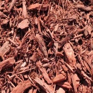 A pile of reddish-brown wood chips scattered. The texture is rough, with varying sizes of shredded pieces, used for landscaping or gardening.