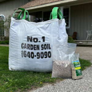 Large white bag labeled "No. 1 Garden Soil" sits on grass. Two smaller bags of soil are next to it near a house.