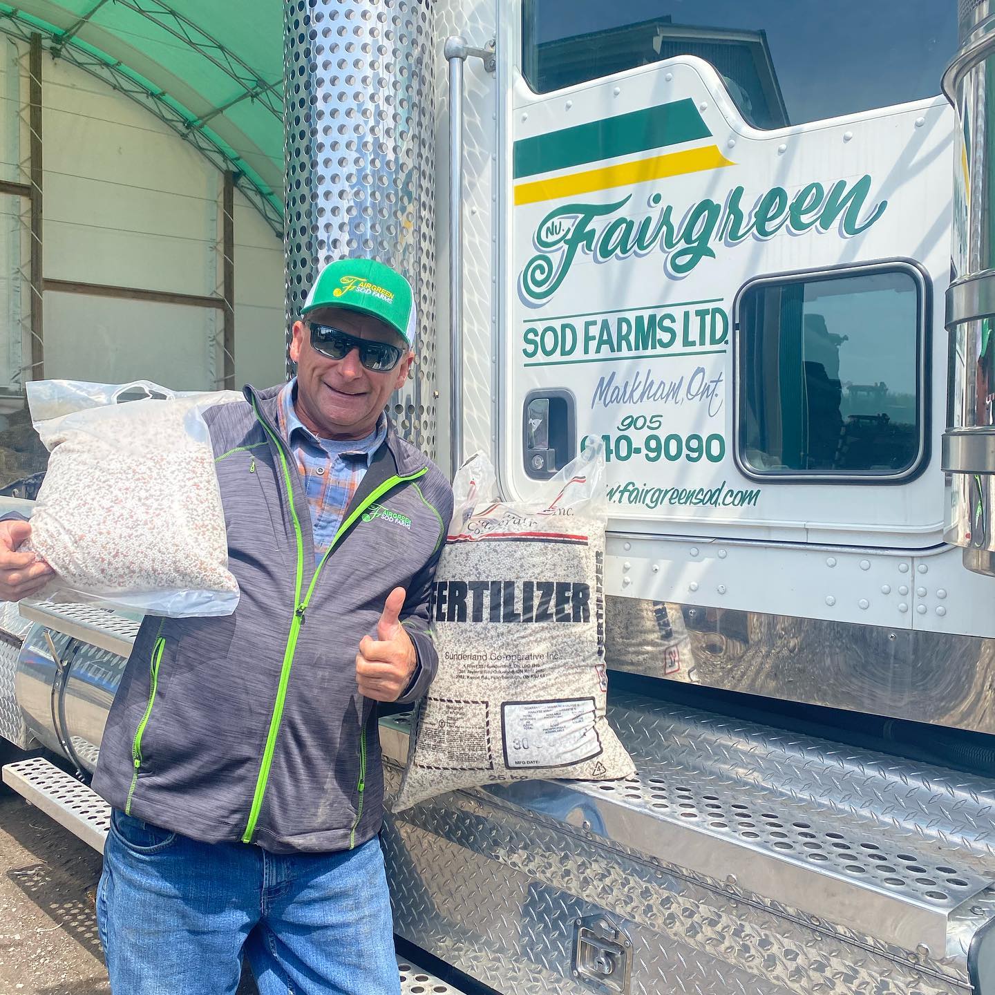 A person stands by a truck labeled "Fairgreen Sod Farms," holding bags of granules and fertilizer, giving a thumbs-up gesture.