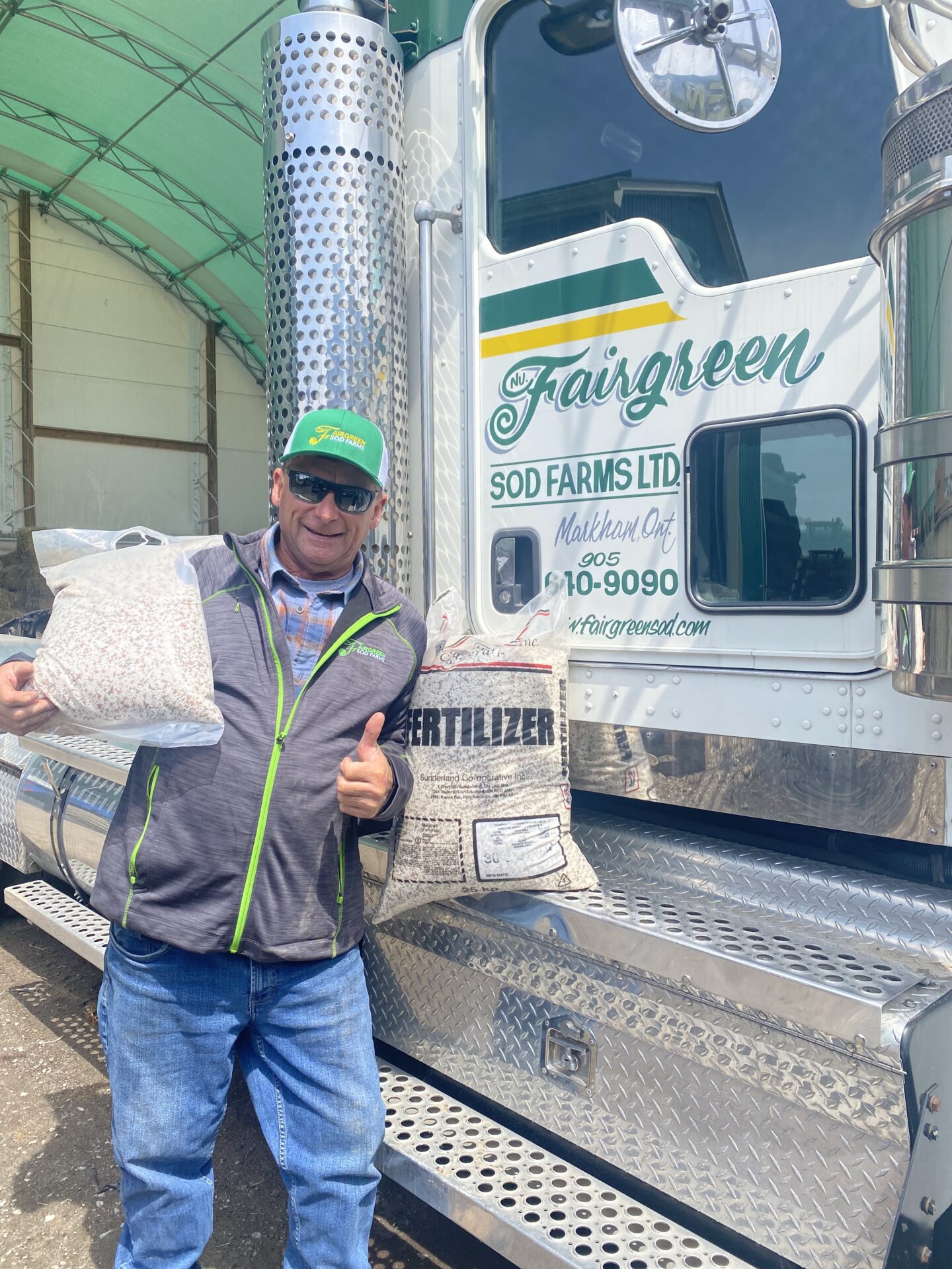 A person holding bags of fertilizer stands next to a truck with "Nutraturf Fairgreen Sod Farms Ltd." printed on its side.