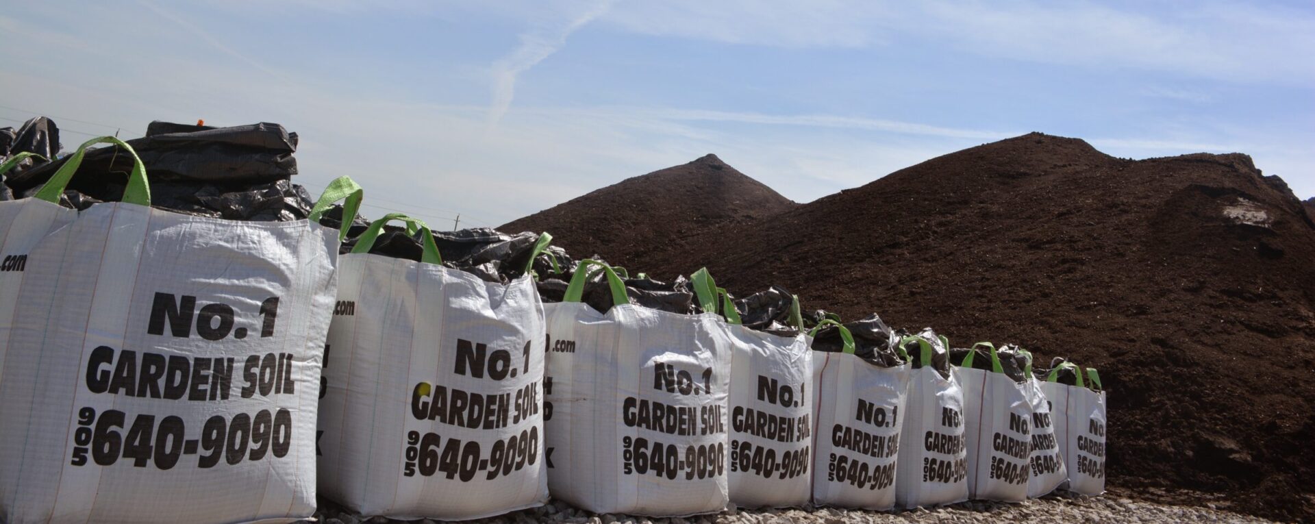 Large bags labeled "No. 1 Garden Soil" lined up beside mounds of soil under a clear sky, suggesting an outdoor gardening or landscaping scene.