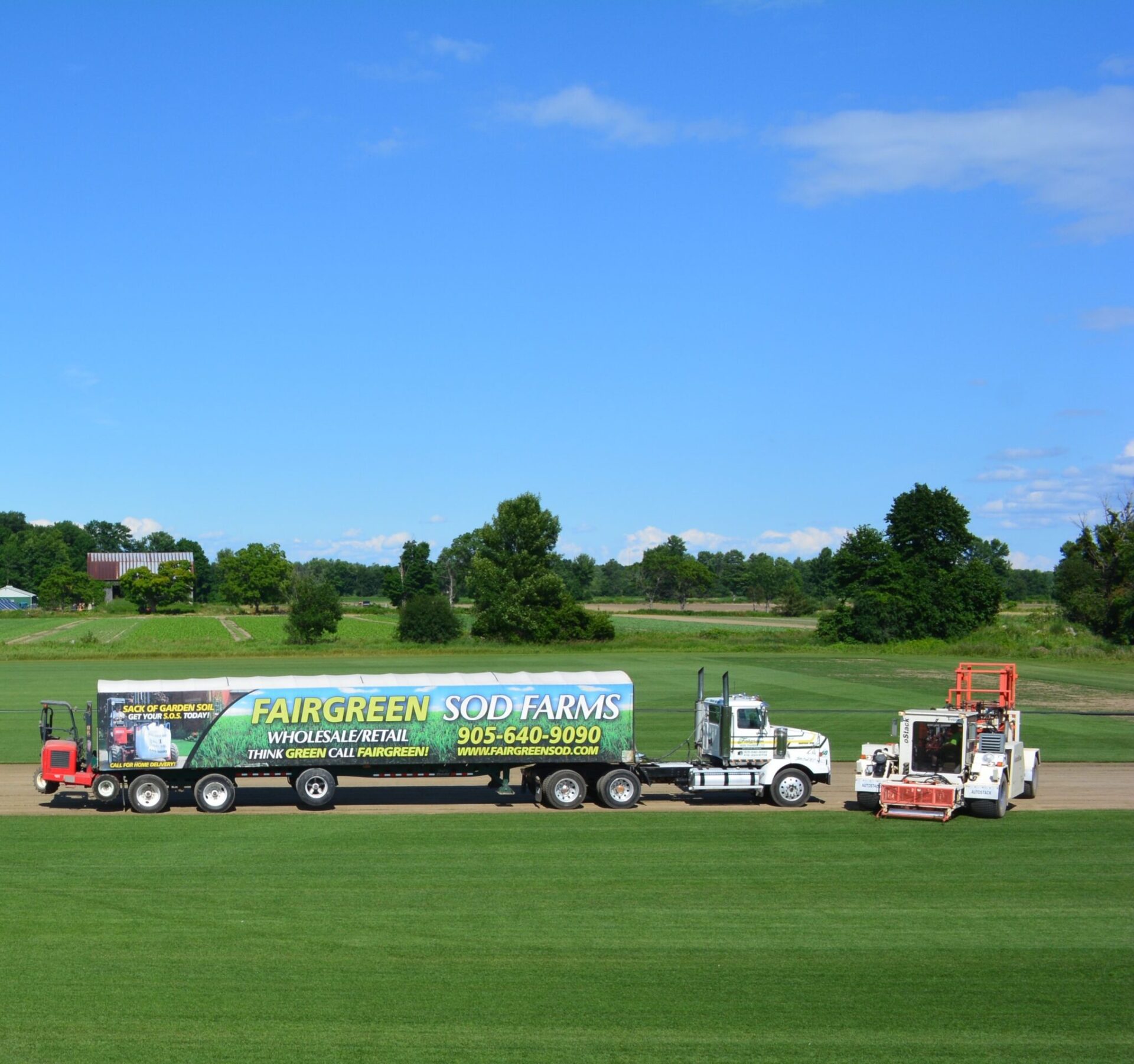 A truck labeled "Fairgreen Sod Farms" is parked on a lush field under a clear blue sky, with trees and a barn in the background.