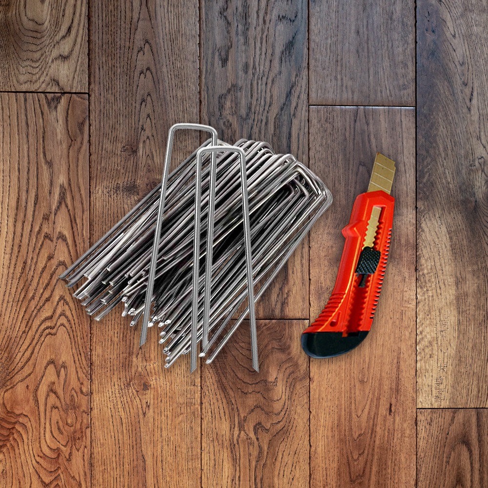 A pile of metal stakes next to a red utility knife lies on a wooden floor, ready for use in construction or gardening.