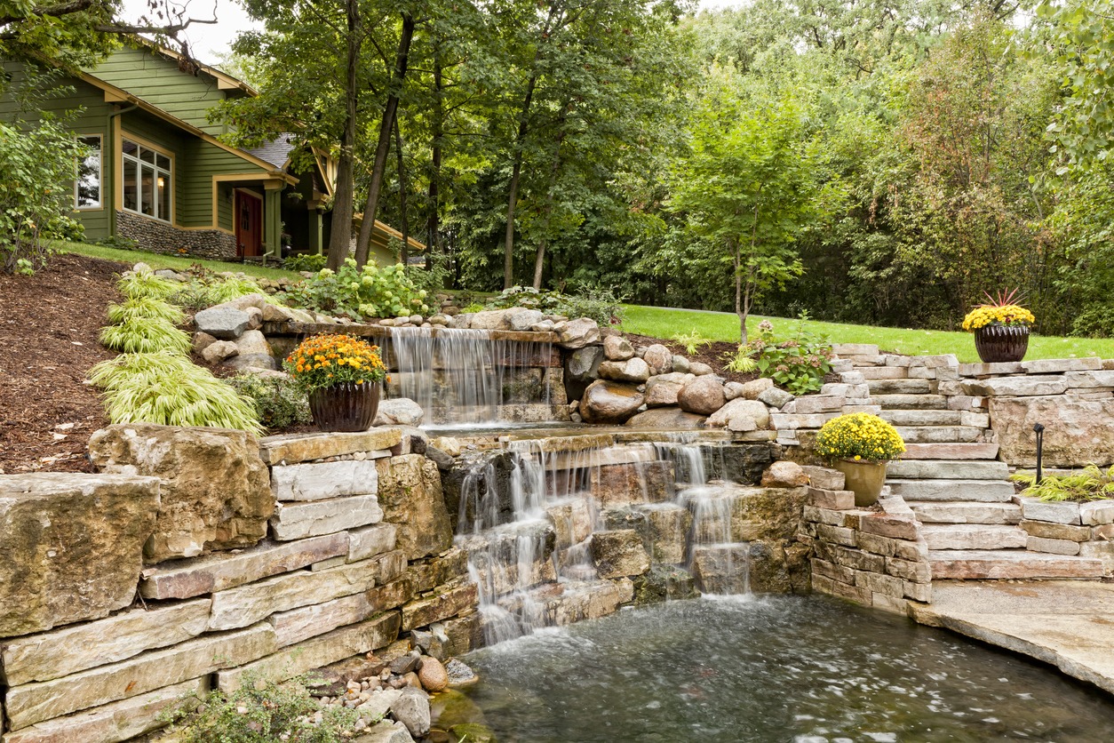 A backyard with a waterfall and a green garden.