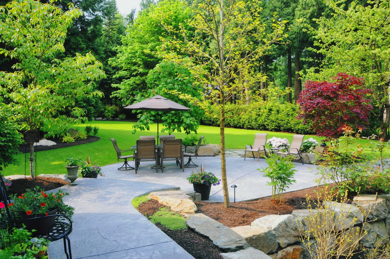 A beautiful backyard garden space with custom stone patio and a lush green lawn.